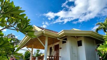 A single-story house with a covered porch, surrounded by lush greenery and a clear blue sky.