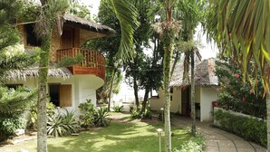 A tropical resort with a thatched-roof building, a balcony, and lush greenery.