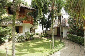 A tropical resort with a thatched-roof building, a balcony, and lush greenery.