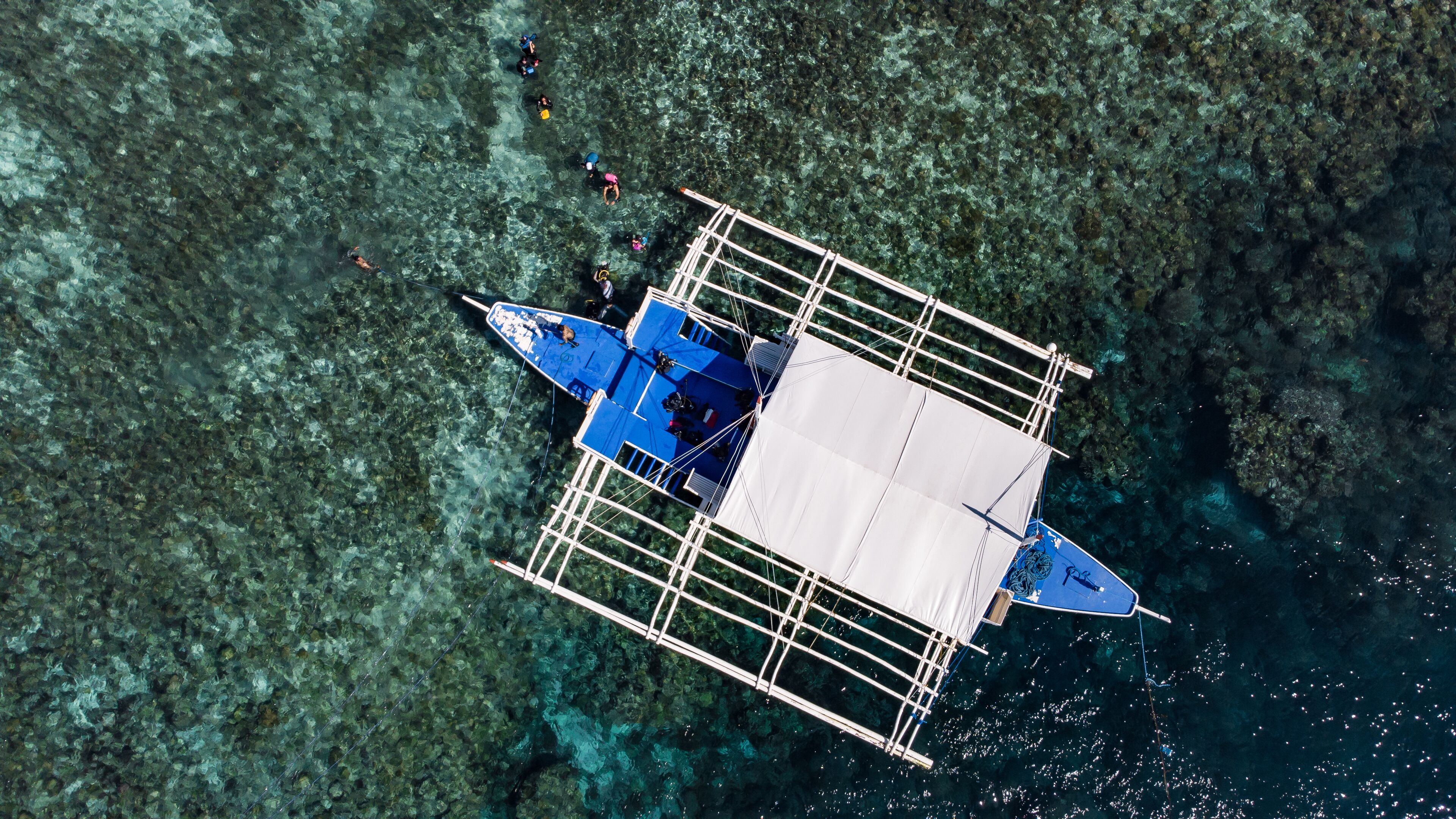 An aerial view of a floating structure with a central open area, surrounded by clear water and a rocky seabed.