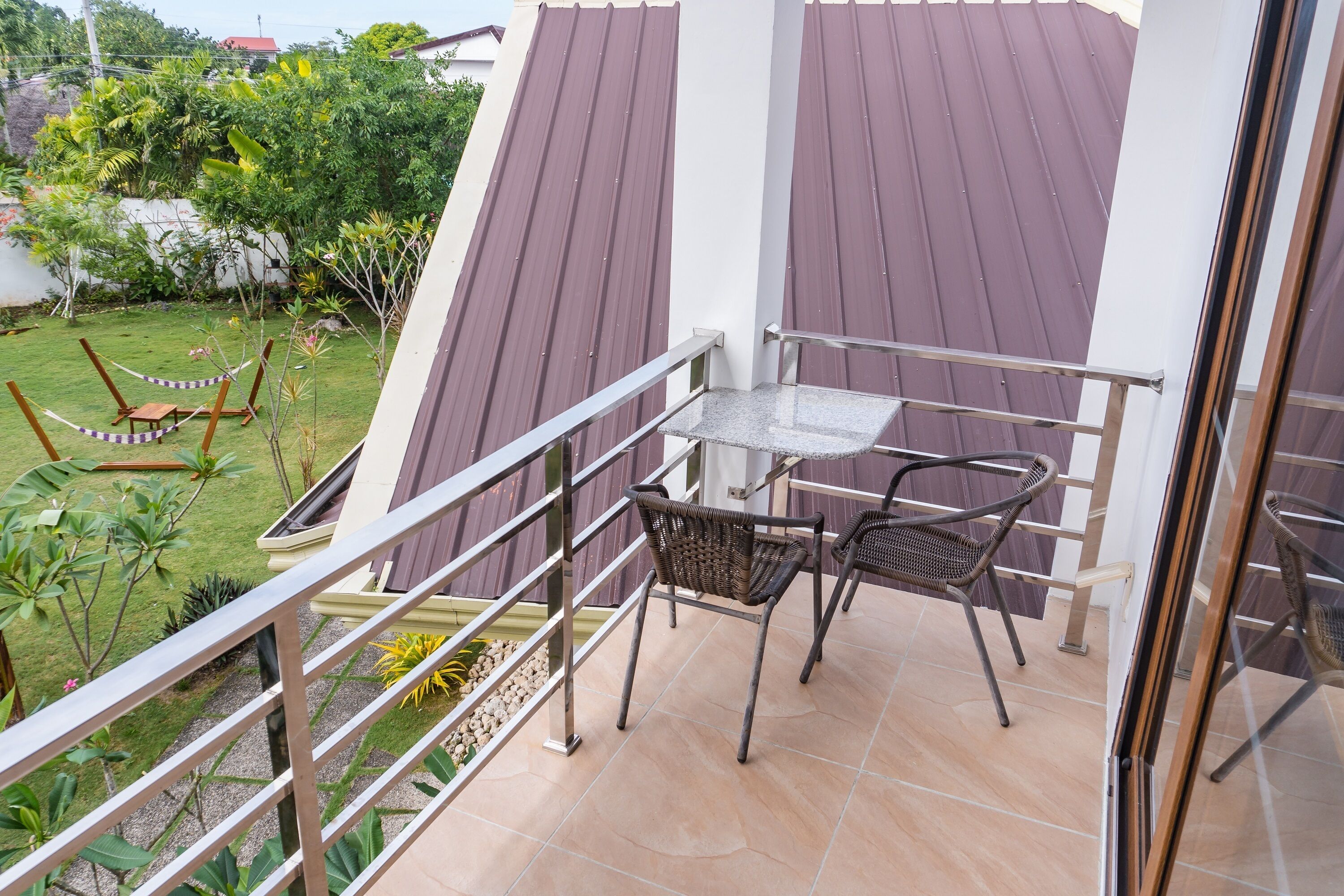 A balcony with a table and chairs, a view of the garden, and a metal railing.