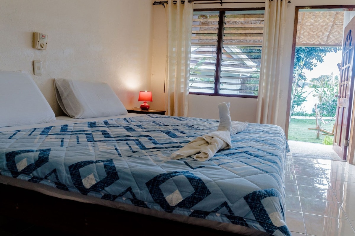 A neatly made bed with a patterned bedspread, a bedside lamp, and a view of the outdoors through a window.