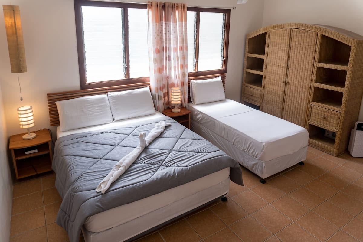 Een kamer met twee bedden, een houten garderobe en een raam met gordijnen.