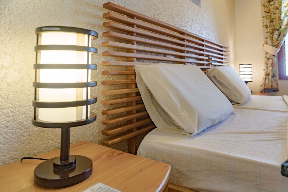 A bed with wooden slats, a bedside lamp, and a nightstand with a lamp.