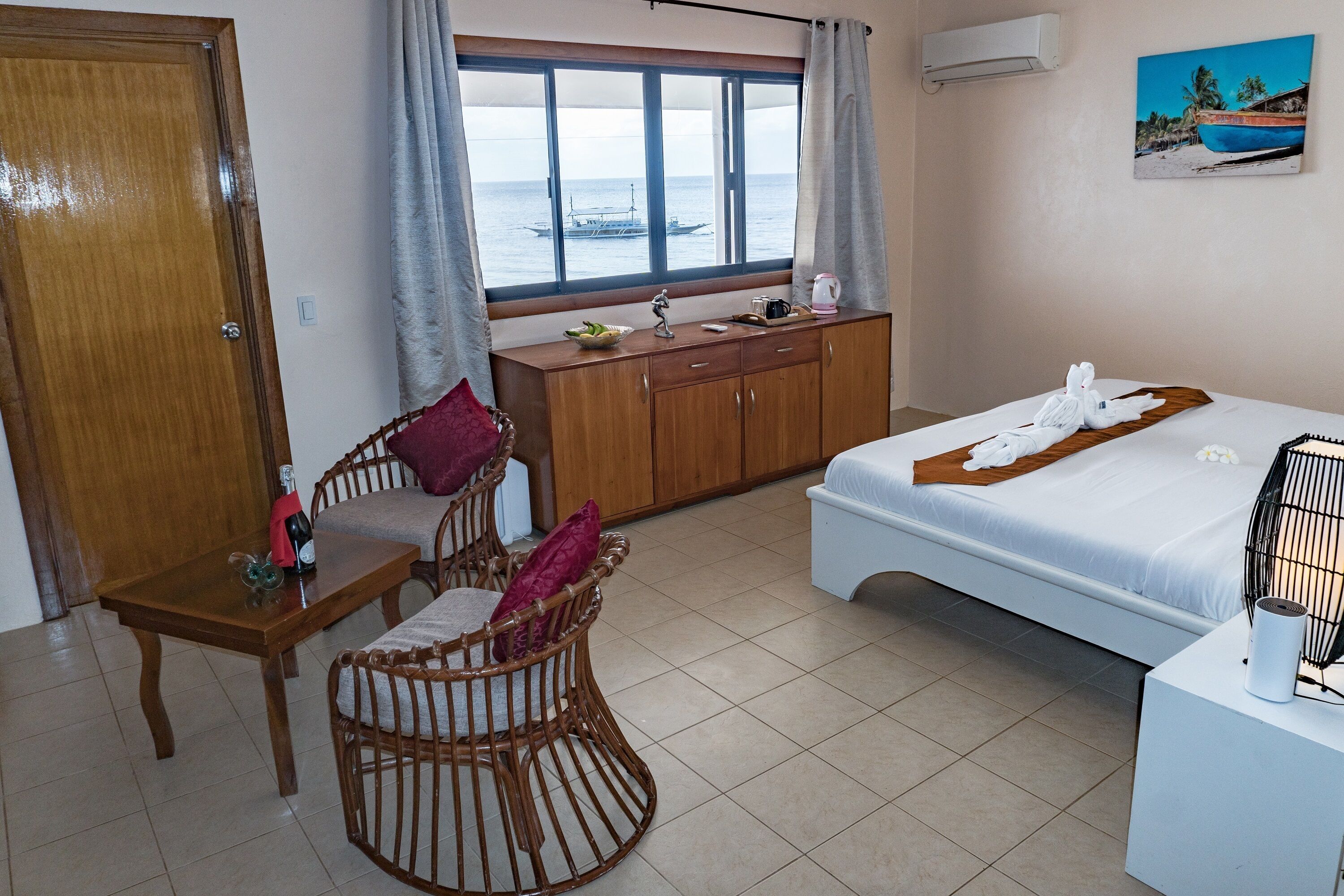 Una habitación con cama, cómoda de madera, mesa de comedor con sillas y ventana con vista al mar.