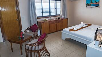 Una habitación con cama, cómoda de madera, mesa de comedor con sillas y ventana con vista al mar.