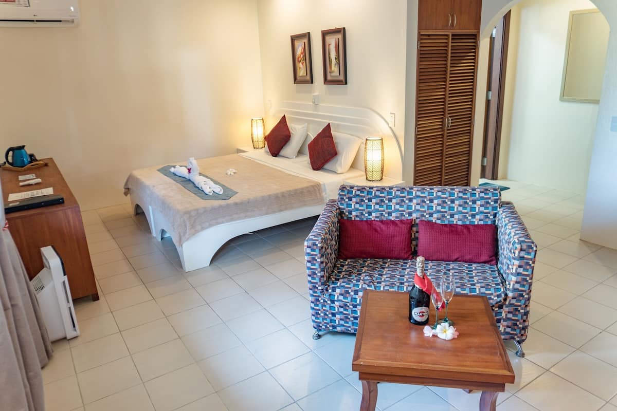 Een hotelkamer met een bed, een bank, een houten tafel met een fles en glazen, en een bureau met een waterkoker en afstandsbedieningen.