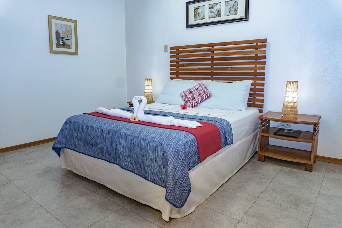 Een keurig opgemaakt bed met een houten hoofdeinde, een blauw-rode spreideken en twee bedlampjes.