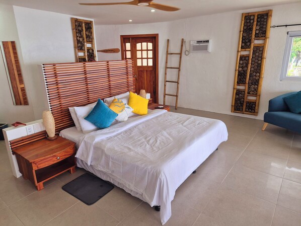 A bedroom with a bed, wooden headboard, bedside tables, a desk, a chair, a ladder, an air conditioning unit, and decorative wooden panels.