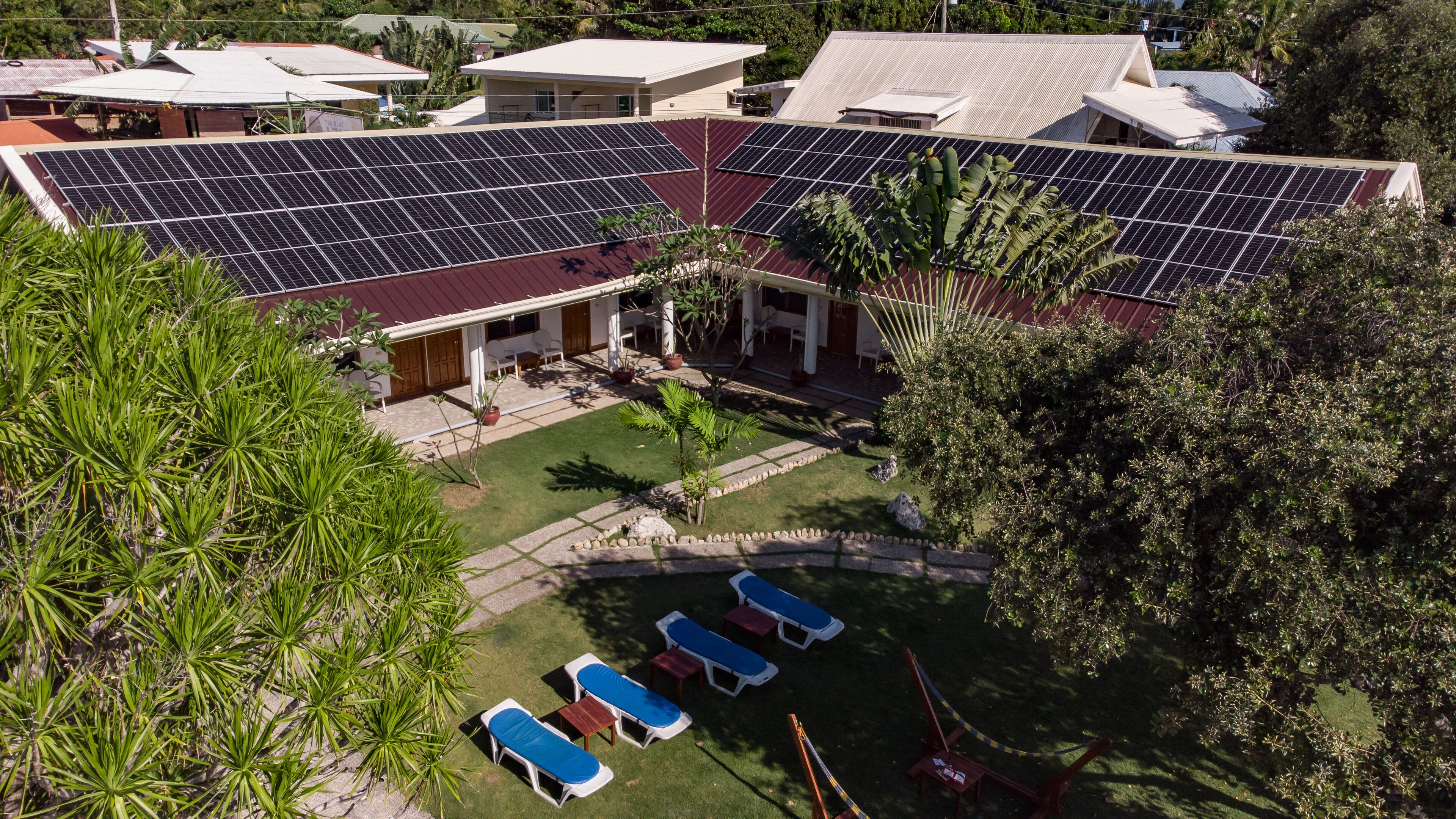 A residential building with solar panels on the roof, a covered patio with lounge chairs, and a well-maintained lawn.