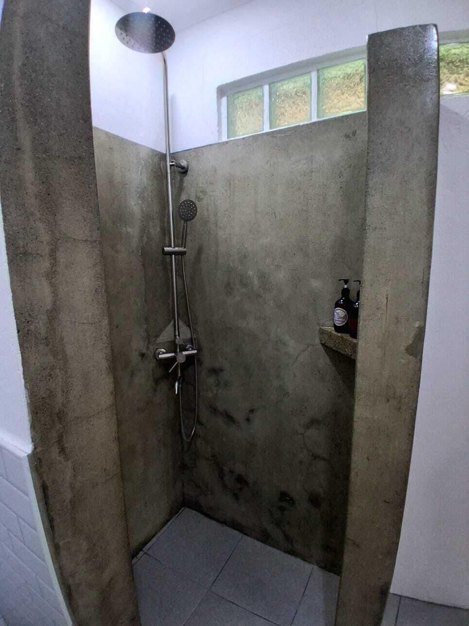 Un área de ducha pequeña y cerrada con cabezal de ducha manual y cepillo manual.