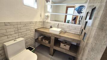 A bathroom with a toilet, a sink, and a mirror. There are baskets under the sink and a window above the toilet.