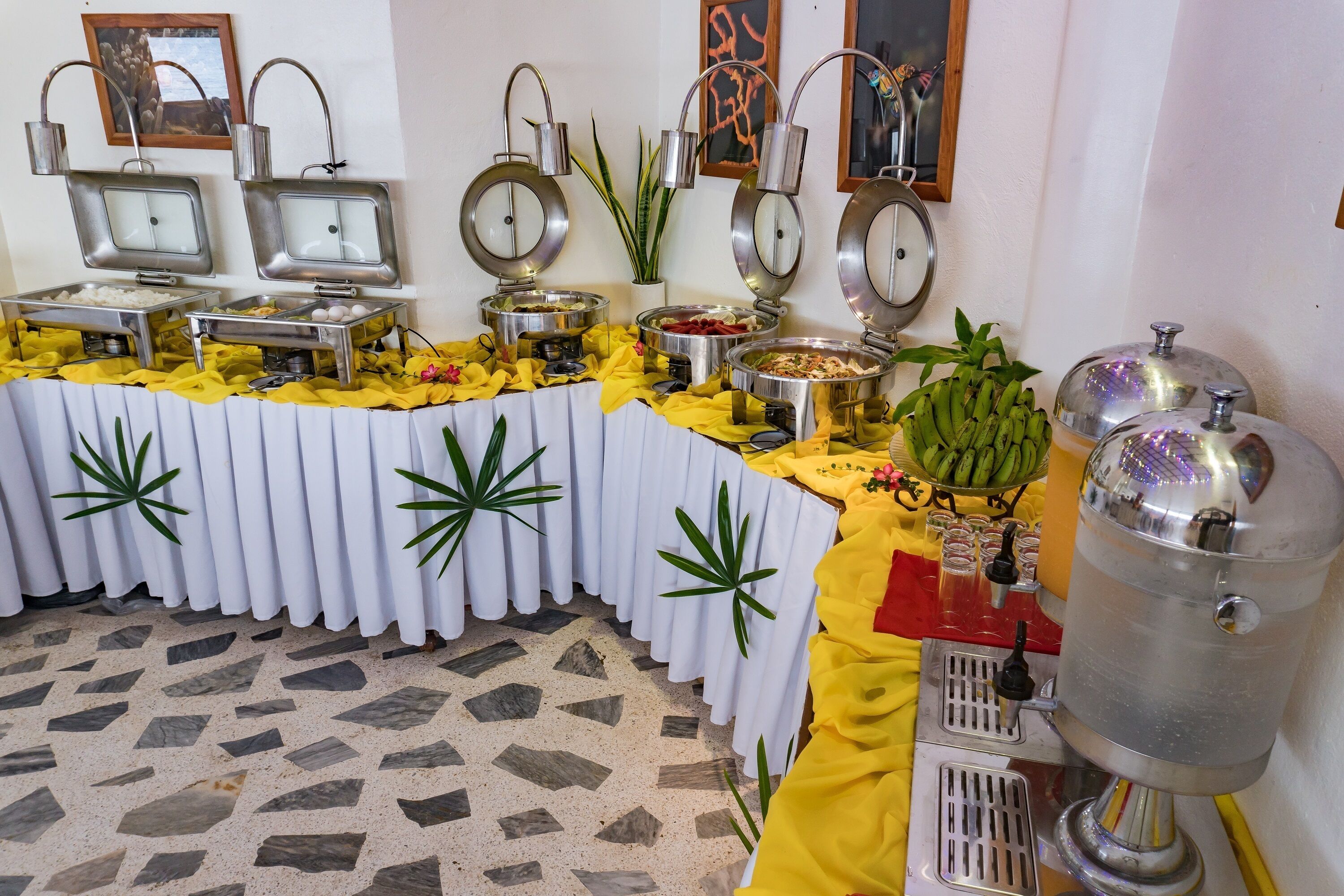 Montaje tipo bufé con diferentes estaciones de comida, dispensador de agua y plantas decorativas.