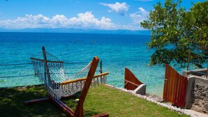 A hammock on a grassy area overlooking a clear blue sea with distant mountains.