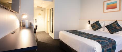 A hotel room with a bed, a desk, and a chair. There is a window with a view of the sky and a painting on the wall.
