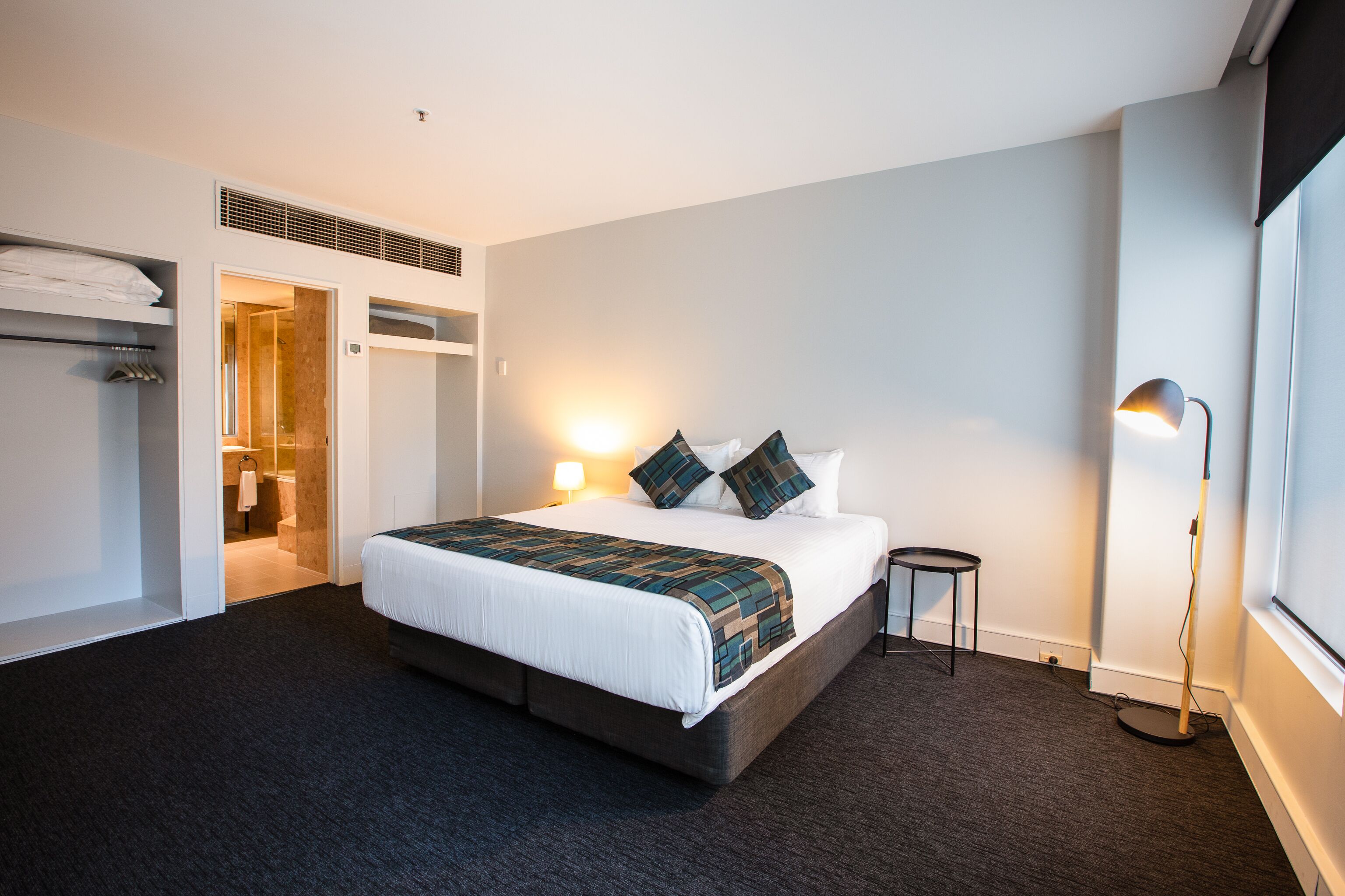 Ein Hotelzimmer mit einem großen Bett, einem Nachttisch, einer Stehlampe und einem begehbaren Kleiderschrank.