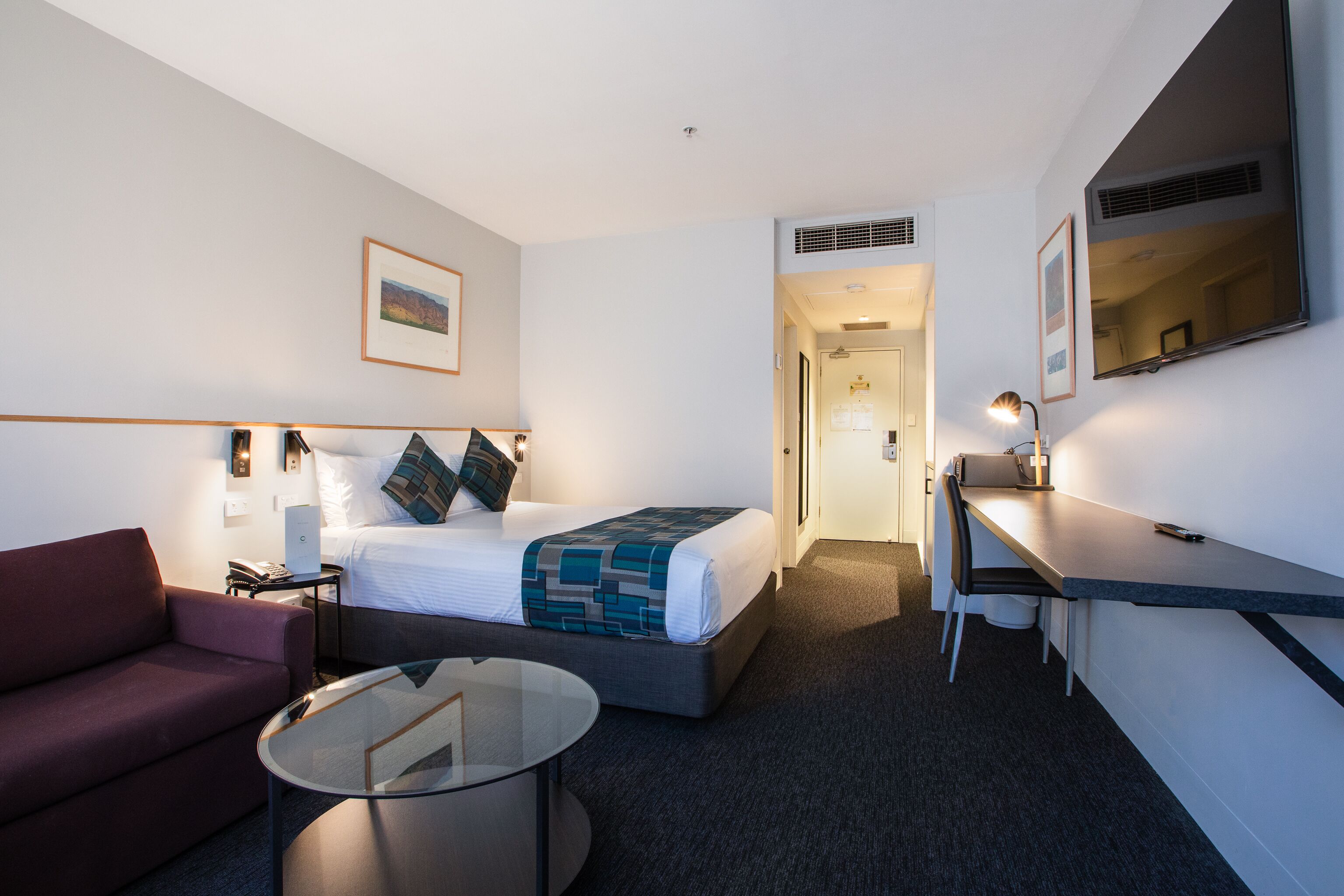 A hotel room with a bed, a desk, a chair, a couch, and a glass coffee table.