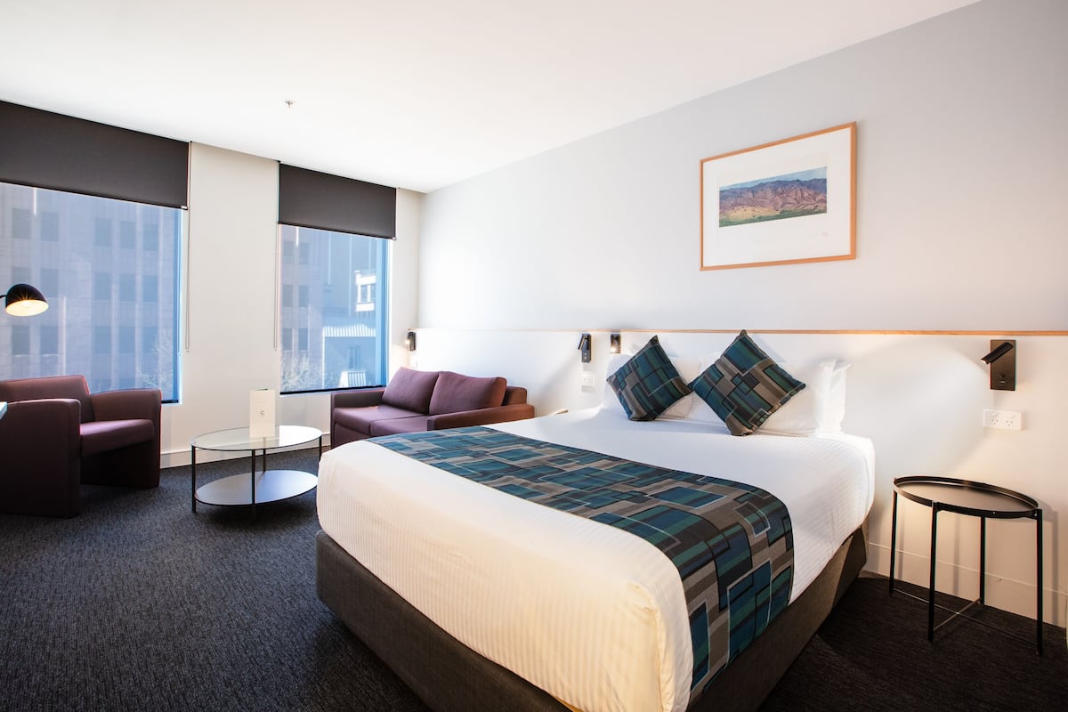 A hotel room with a large bed, two armchairs, a small table, and a large window.