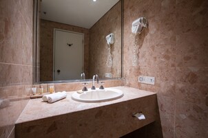 Un baño con lavamanos, espejo, secador de pelo y artículos de aseo.