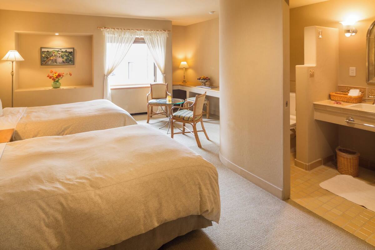 Hotellihuone, jossa on kaksi sänkyä, työpöytä, tuoli, lamppu, taulu ja kylpyhuone.