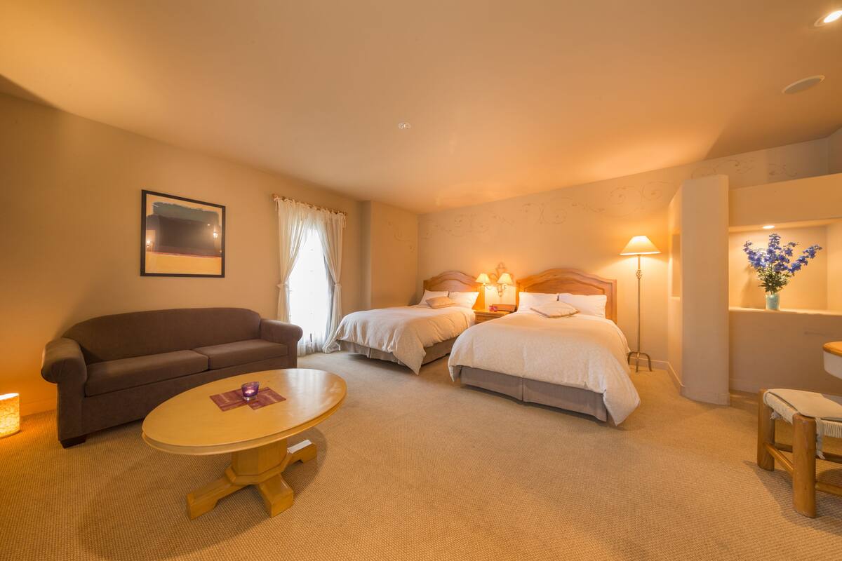 Hotellihuone, jossa on kaksi sänkyä, sohva, pyöreä pöytä ja pieni työpöytä.