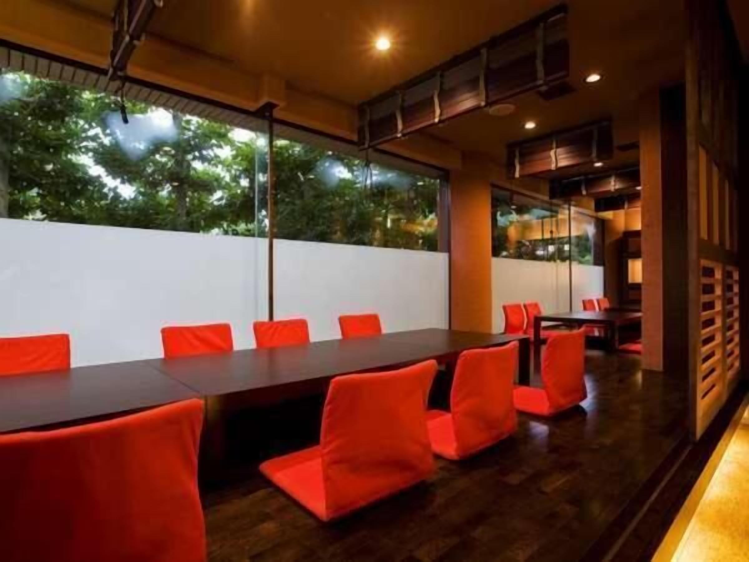 A conference room with a long table and red chairs, large windows with a view of trees, and a modern interior design.