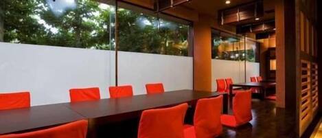 A conference room with a long table and red chairs, large windows with a view of trees, and a modern interior design.