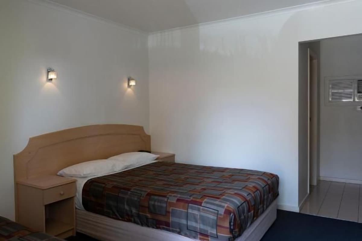 A small, simple room with a single bed, a nightstand, and two wall-mounted lights.