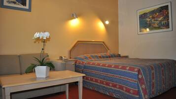 A hotel room with a bed, a sofa, a small table, a nightstand, a lamp, and a potted plant.