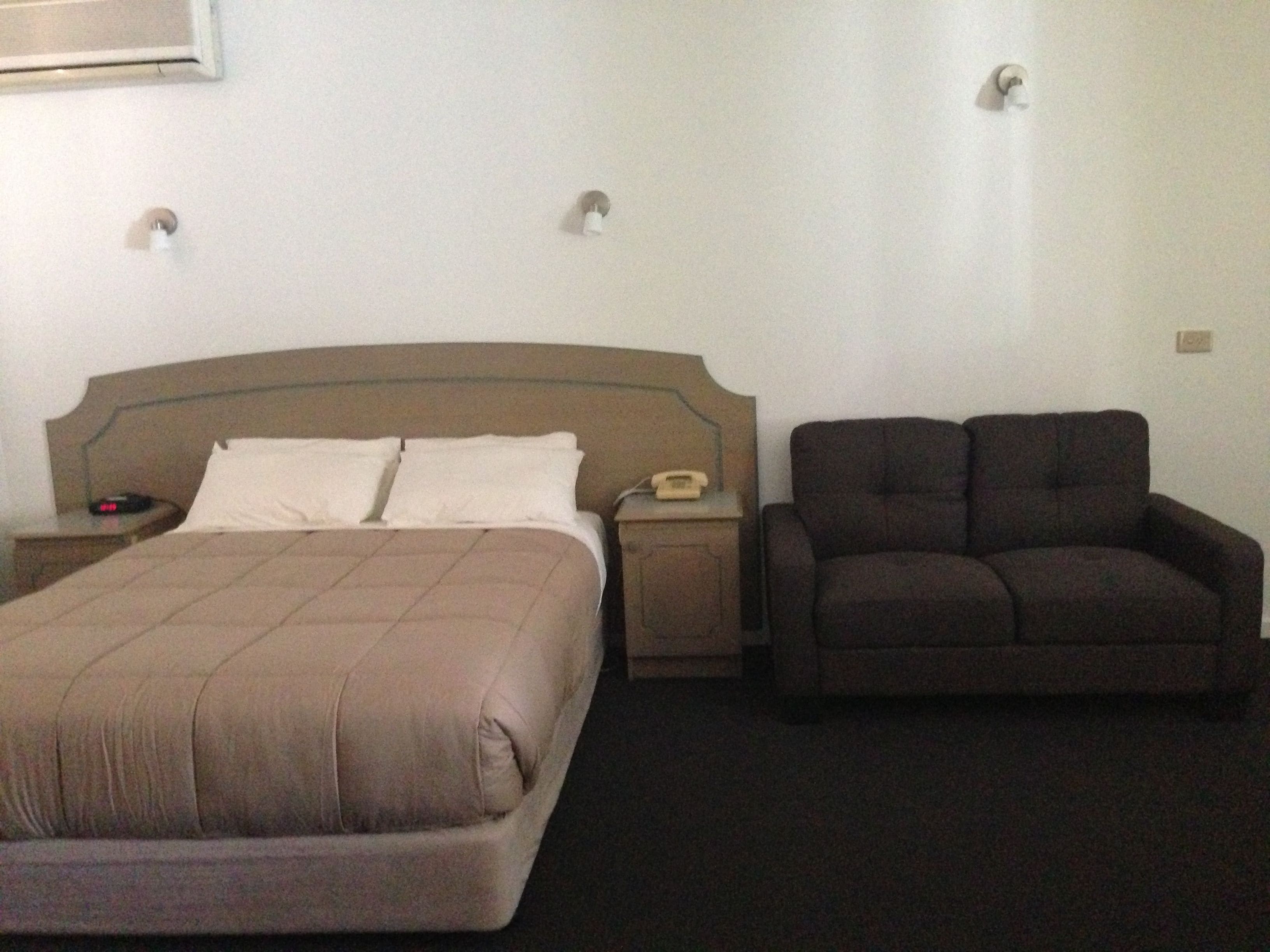 A hotel room with a bed, a nightstand, a telephone, and a sofa.