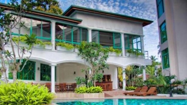 Un edificio moderno con piscina, que presenta un patio cubierto con mobiliario y abundante vegetación.