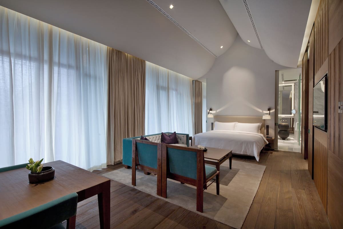 Une chambre d’hôtel moderne comprenant un lit, un coin salon avec une table et une grande fenêtre avec des rideaux.