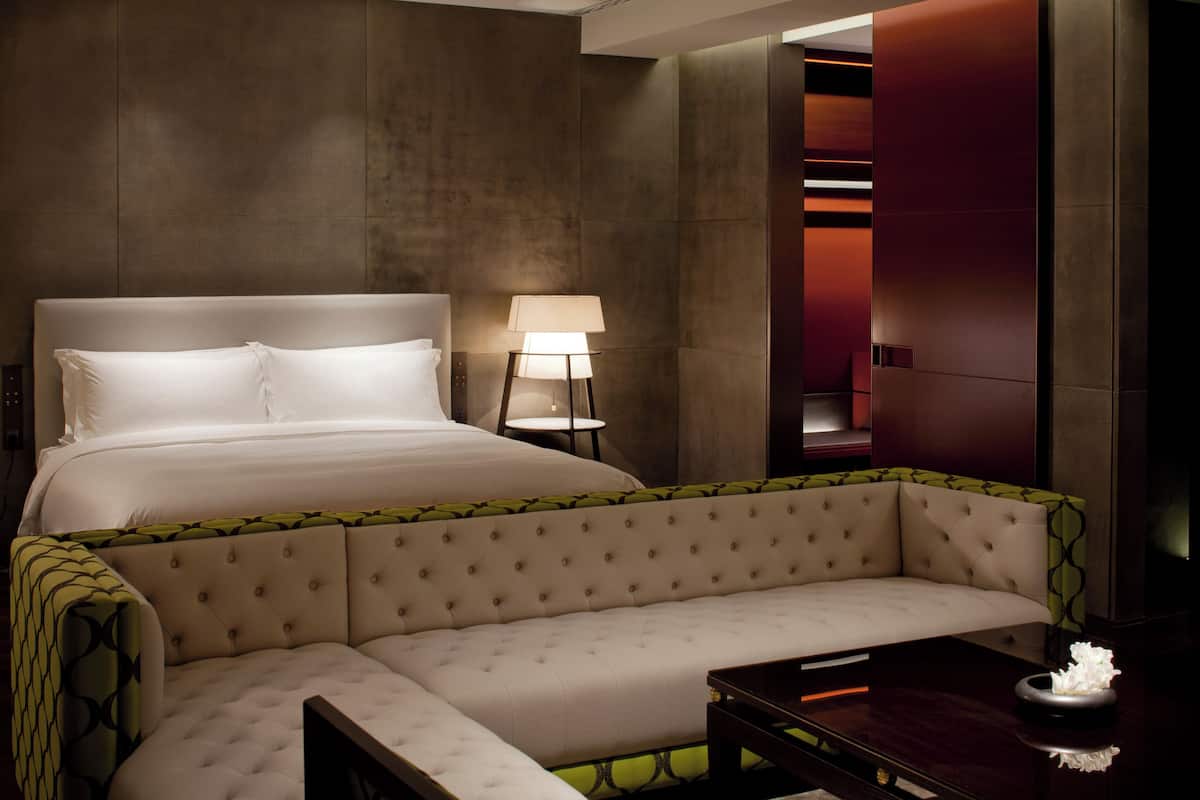 Une chambre d’hôtel moderne avec un grand lit, un canapé, une table d’appoint et une lampe.