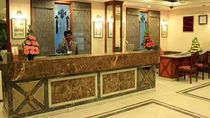 A hotel reception area with a marble counter, framed artwork, and a seating area with chairs. - Hotel Basant Residency (Bengaluru)