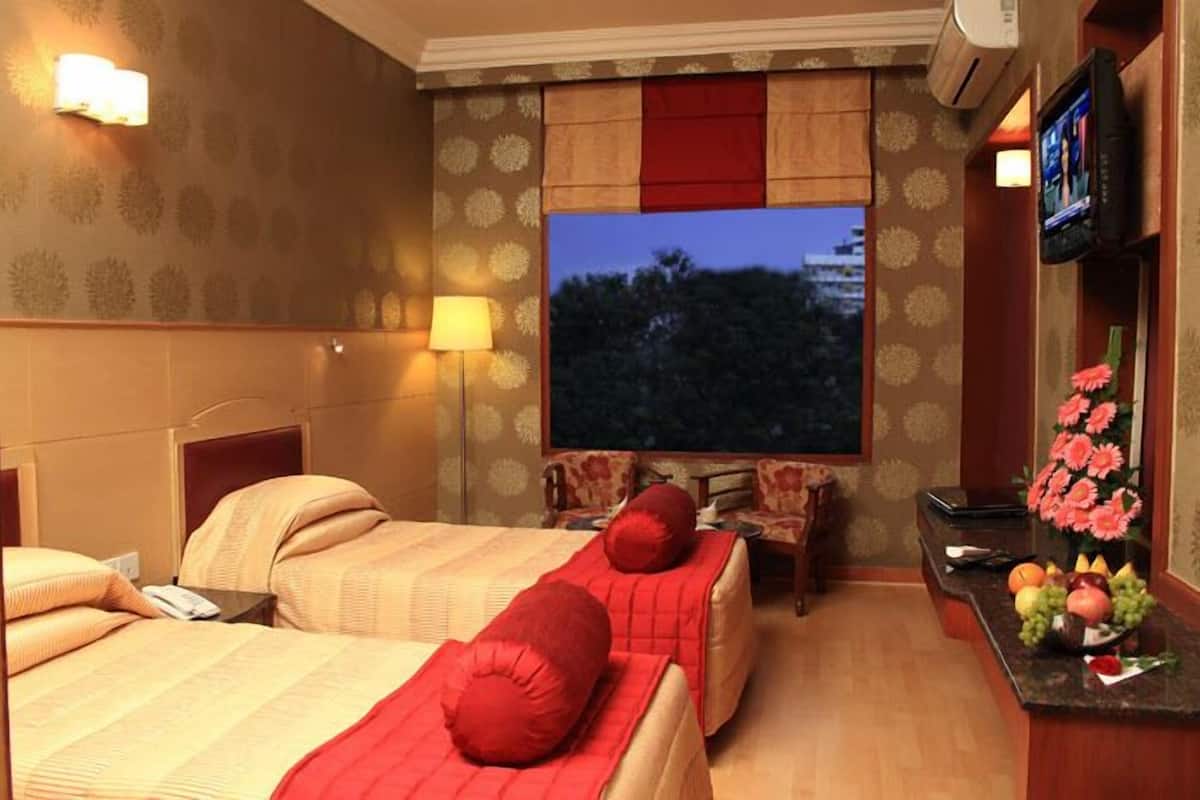 A hotel room with two beds, a TV, a desk with a computer, and a flower vase.