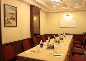 A conference room with a long table, red chairs, water bottles, and a whiteboard. - Hotel Basant Residency (Bengaluru)