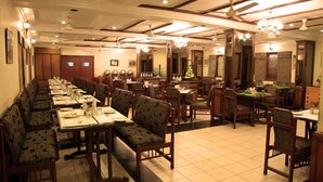 A spacious restaurant with high ceilings, chandeliers, and a long counter with booths. - Hotel Basant Residency (Bengaluru)