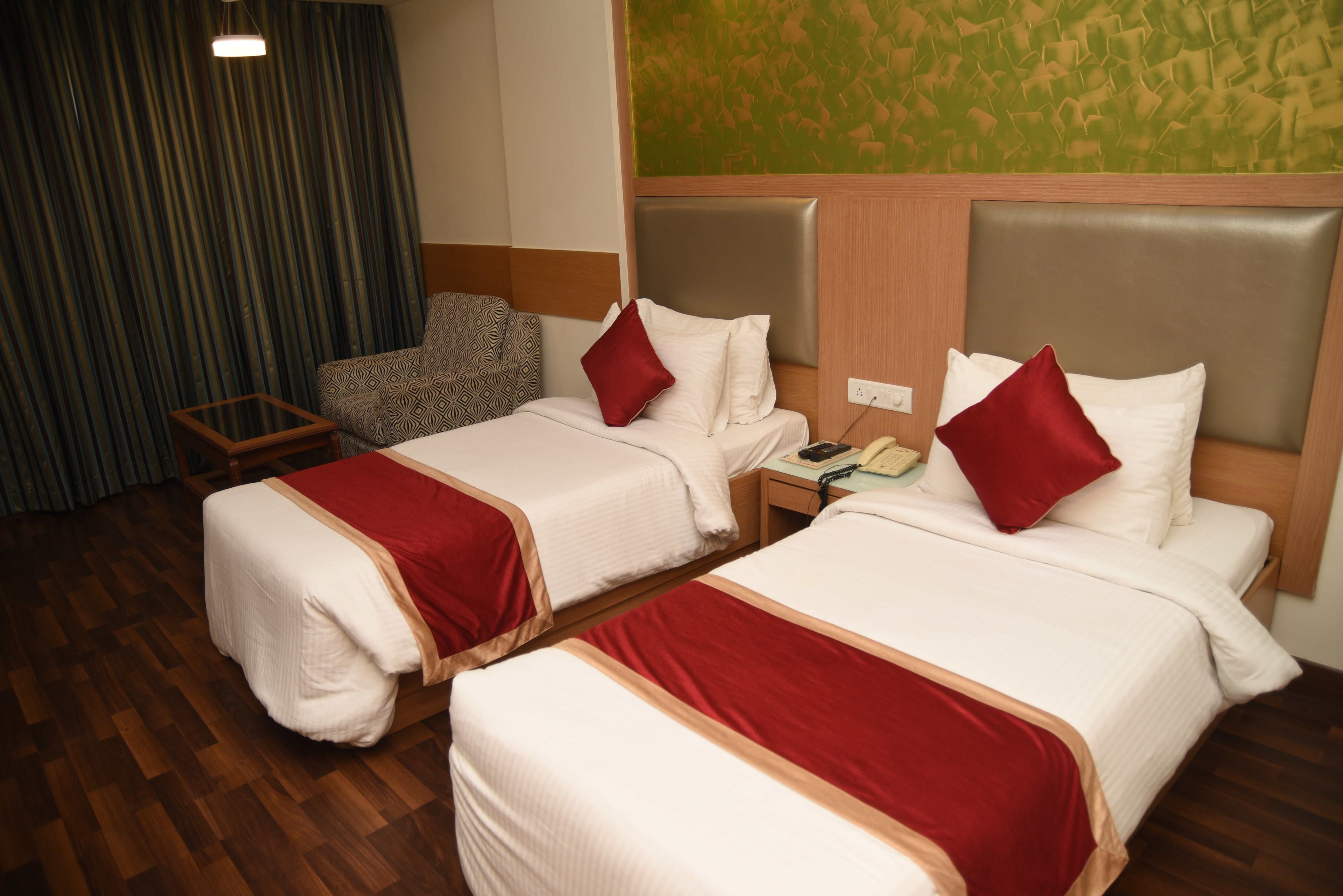 A hotel room with two beds, a nightstand, a chair, and a wooden floor.