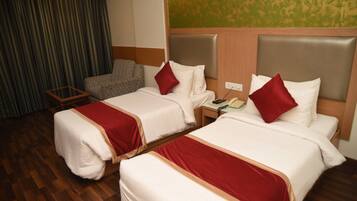 A hotel room with two beds, a nightstand, a chair, and a wooden floor.