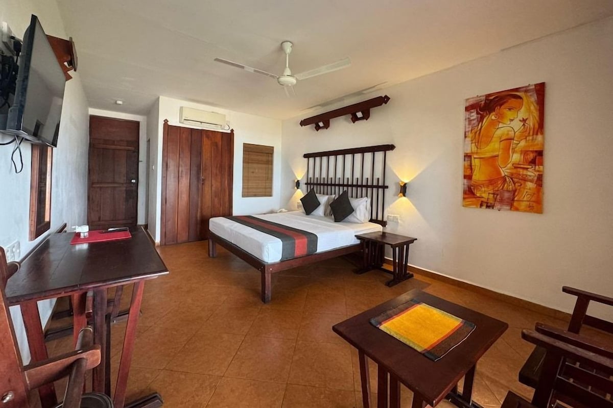 A room with a bed, a desk, a chair, a table, a ceiling fan, and a wall-mounted TV.