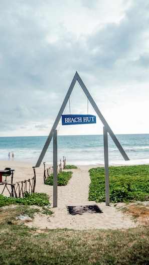 A beach hut entrance with a sign, a sandy path, and the ocean in the background. - The Long Beach Resort (Koggala)