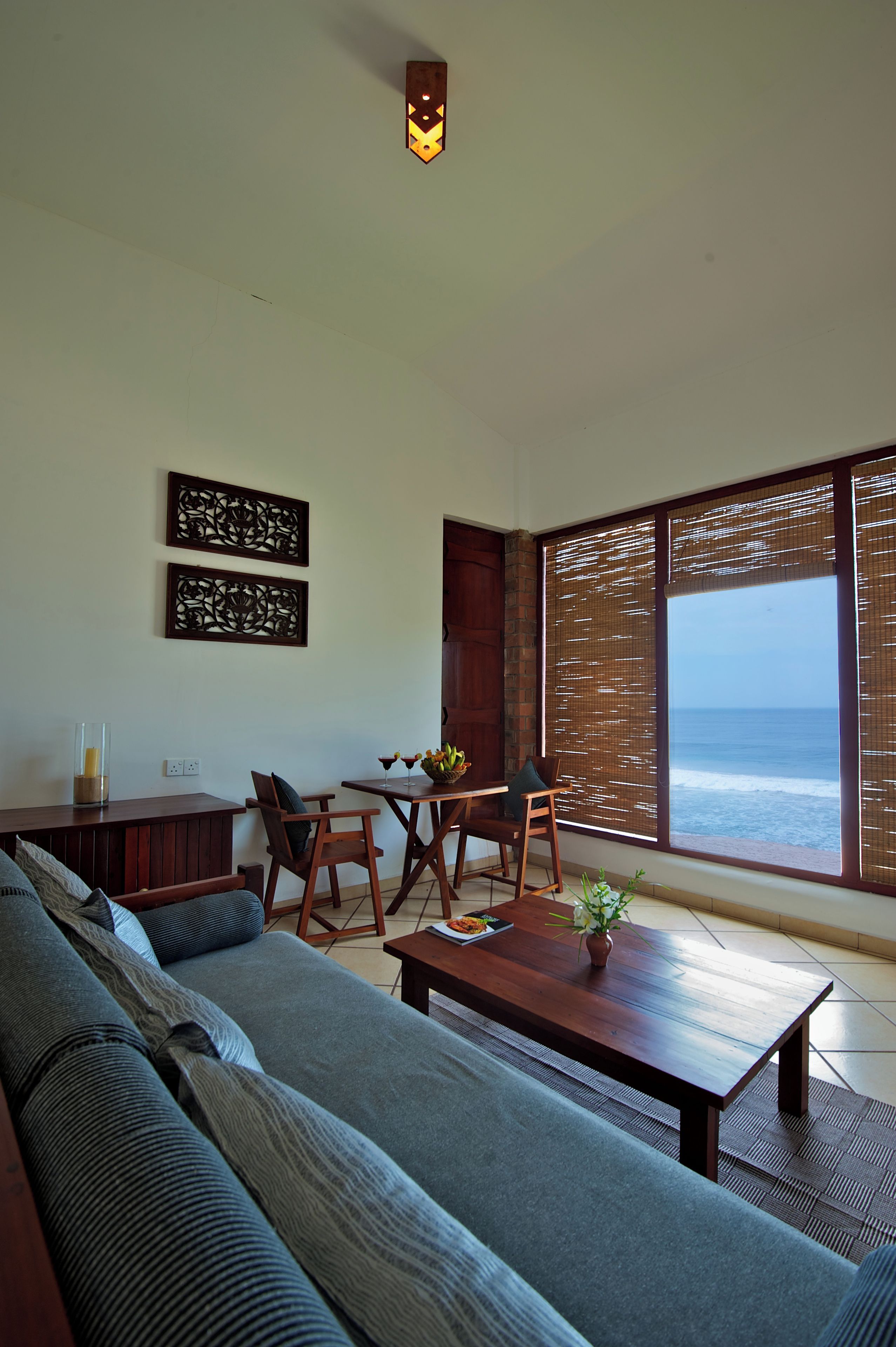 Una sala de estar moderna con un gran ventanal con vista al océano, un sofá, una mesa de comedor con sillas y decoración en la pared.