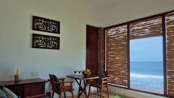 Una sala de estar moderna con un gran ventanal con vista al océano, un sofá, una mesa de comedor con sillas y decoración en la pared.
