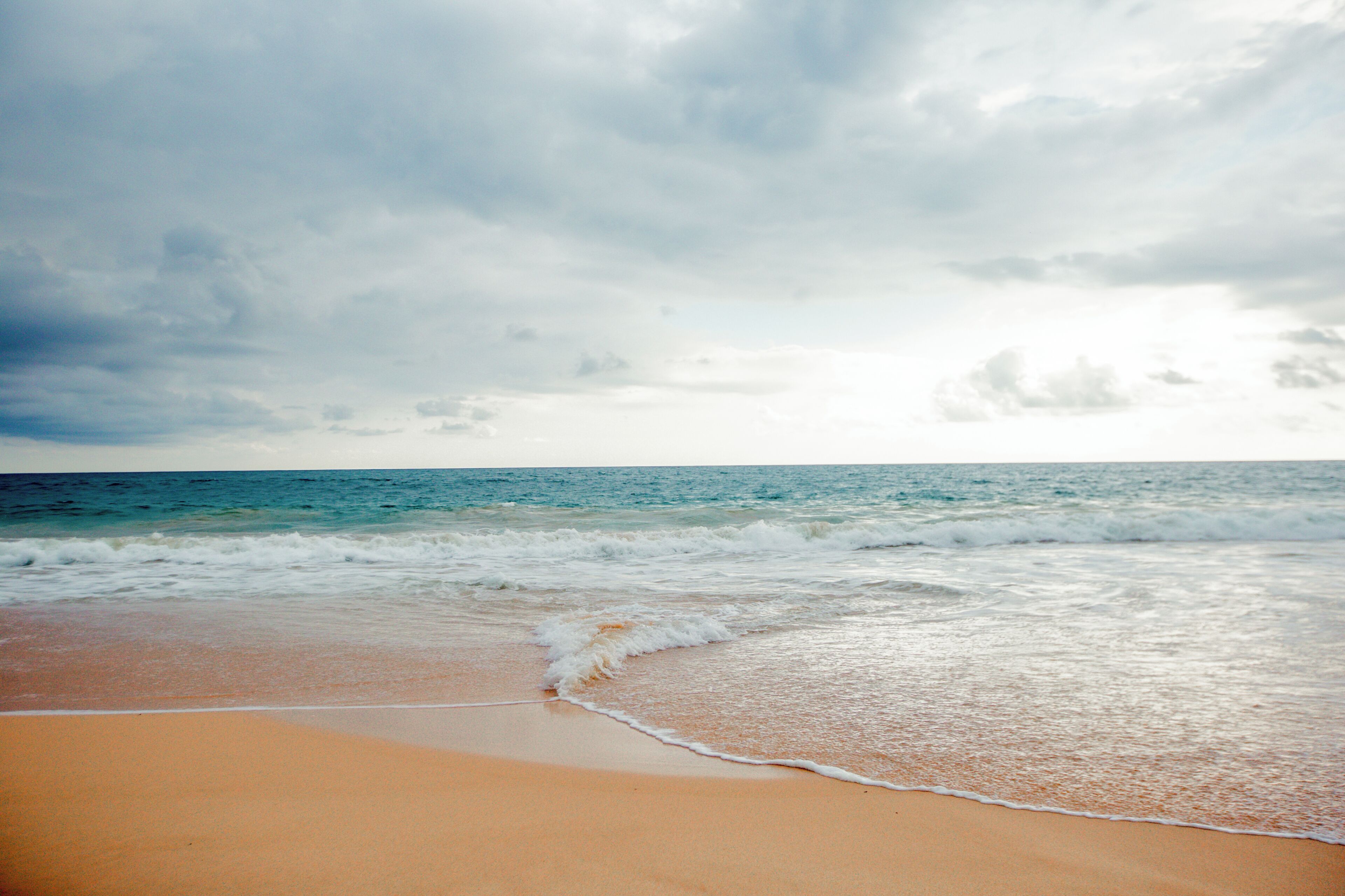 Ein Strand mit Wellen, blauem Himmel und ruhiger See.