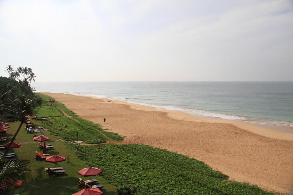 A beach with a person walking, red umbrellas, and greenery.