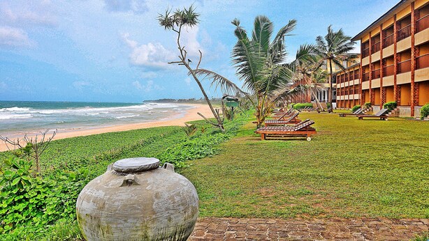 Un hôtel situé en bord de mer, doté d’une piscine, de palmiers et offrant une vue sur l’océan.