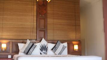 Una habitación de hotel con una cama grande, varios almohadones, un cabecero de madera y lámparas fijadas a la pared.