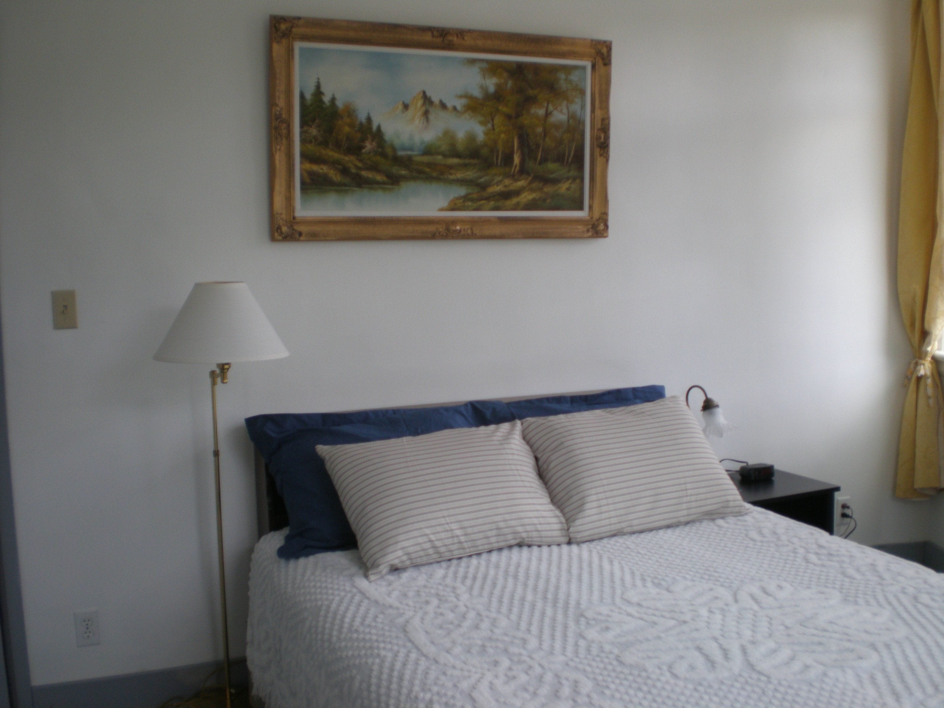 A bedroom with a bed, a nightstand, a lamp, and a painting on the wall.
