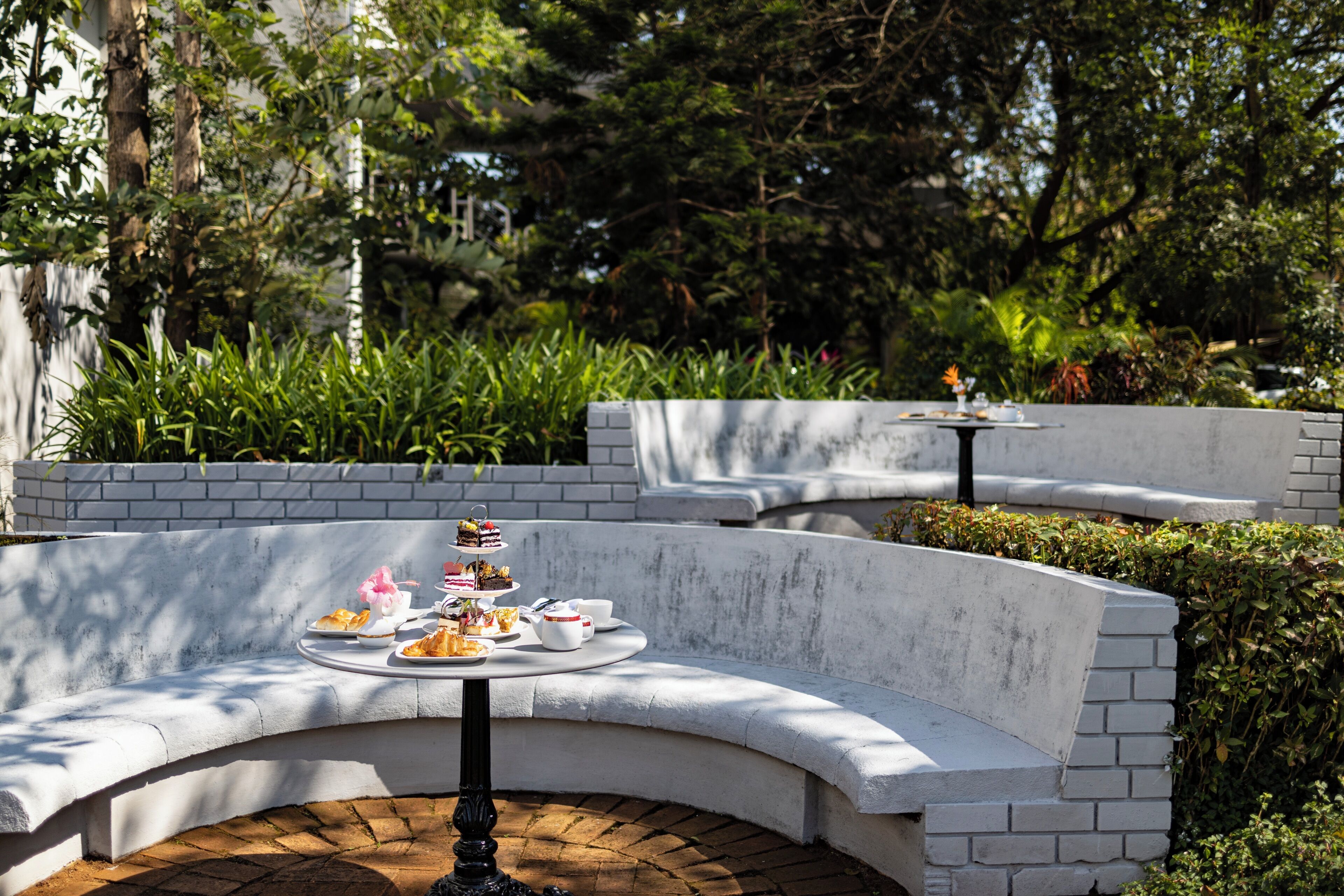 Un área de estar al aire libre con curvas, con una mesa dispuesta para una comida, rodeada de follaje y un muro de ladrillo.