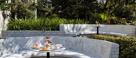 Un área de estar al aire libre con curvas, con una mesa dispuesta para una comida, rodeada de follaje y un muro de ladrillo.